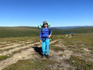 Elisa Montonen rinkka selässä korkealla puurajan yläpuolella Urho Kekkosen kansallispuistossa. Poutainen keli, sininen taivas ja pyöreäpiirteiset tunturien ja vaarojen ääriviivat näkyvät kilometrien päähän.
